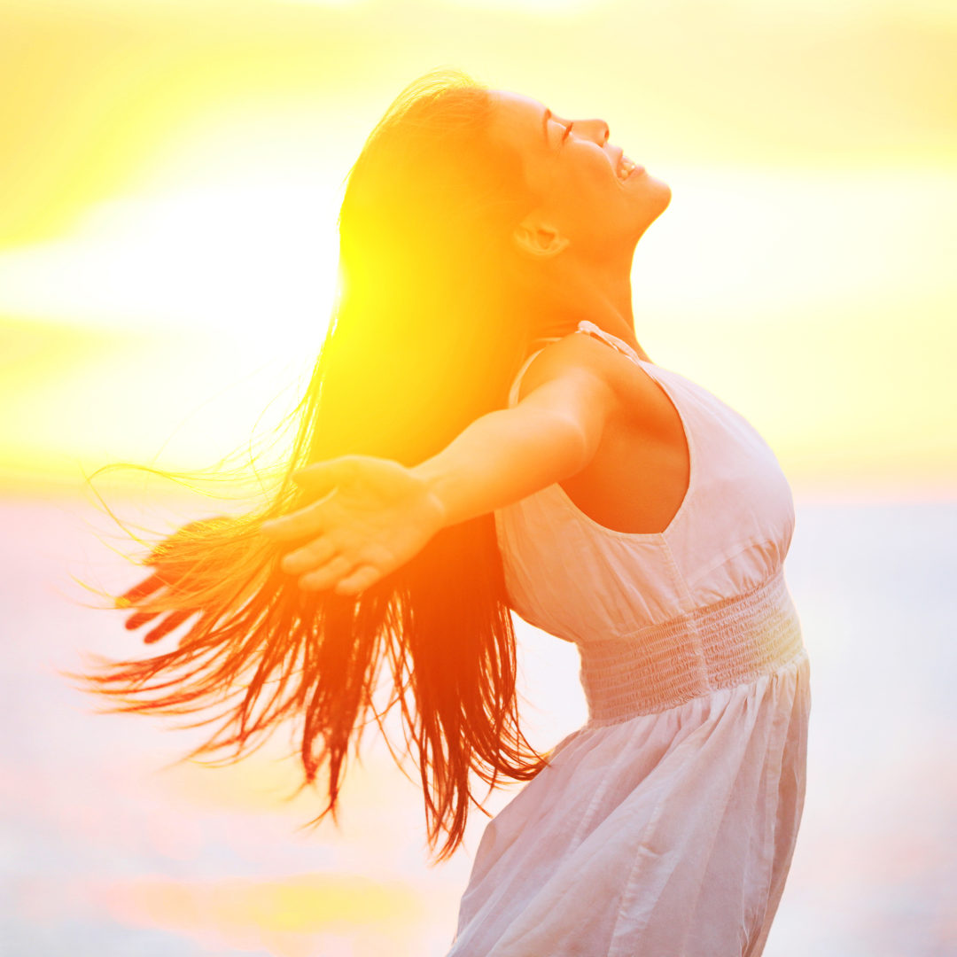 Woman in a white dress with long hair standing against a bright yellow background, she's happy