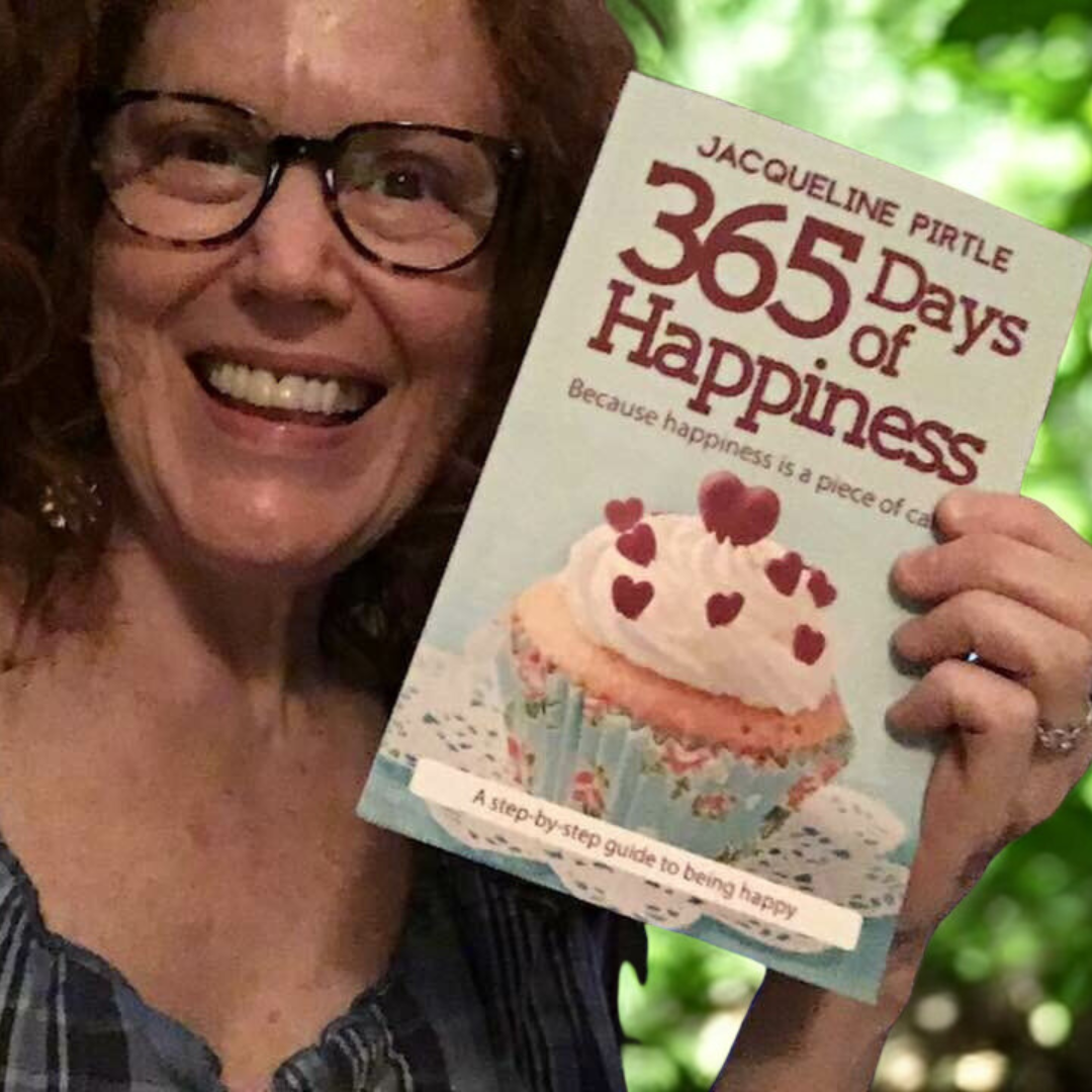 Person holding a book titled '365 Days of Happiness' by Jacqueline Pirrtle with a cupcake illustration on the cover.